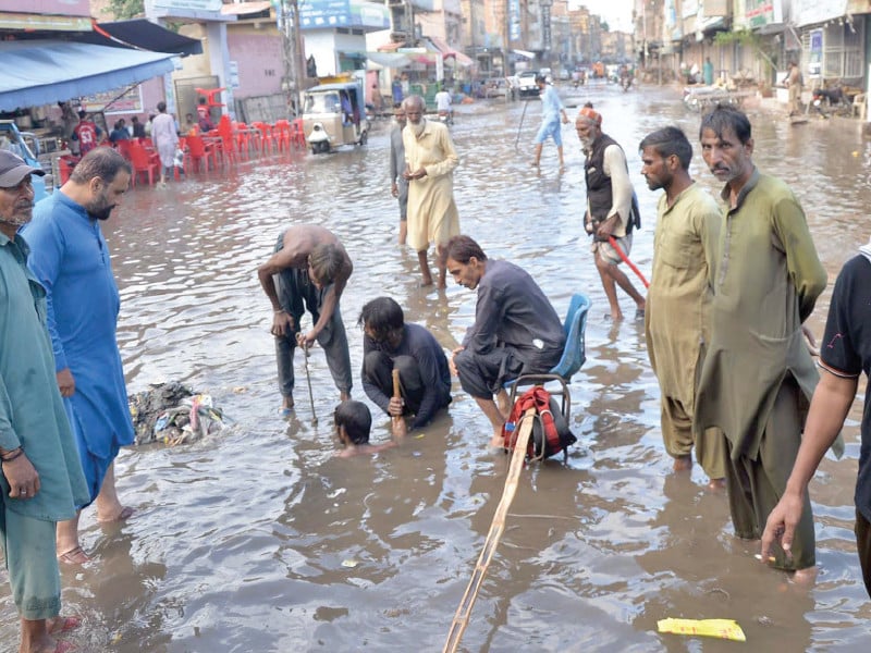 The head sweeper looks prominent sitting on a chair issuing instructions while drain divers try to clear a clogged gutter to allow rainwater to flow out on a street in Hyderabad on Friday. Photo: Express